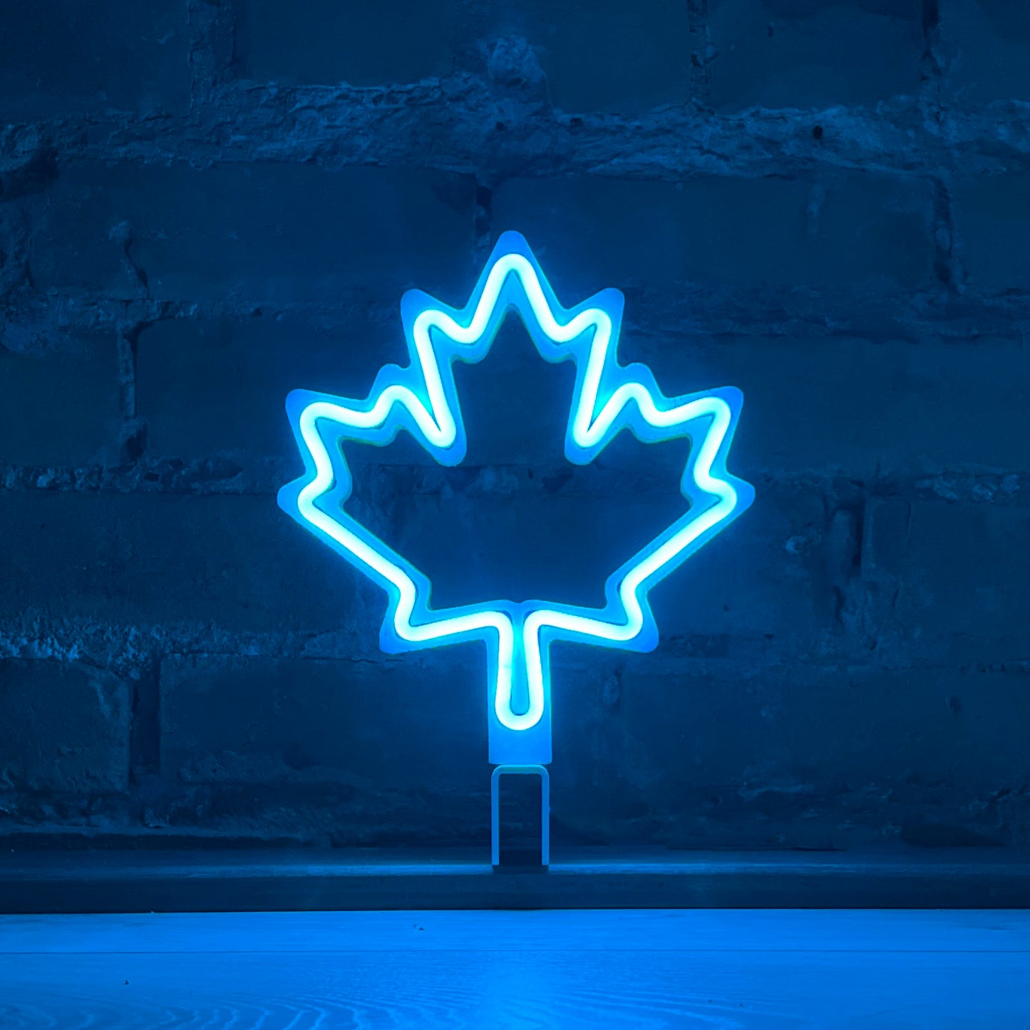 Cyan neon maple leaf art glowing against a brick wall - LED neon maple leaf light by Our Glowing Hearts handmade in Canada