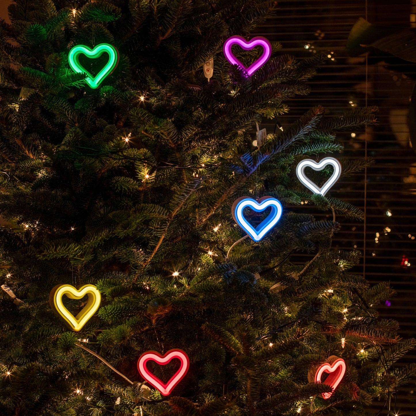 Collection of colorful LED neon heart ornaments on a Christmas tree in green magenta white cyan yellow pink and red by Our Glowing Hearts