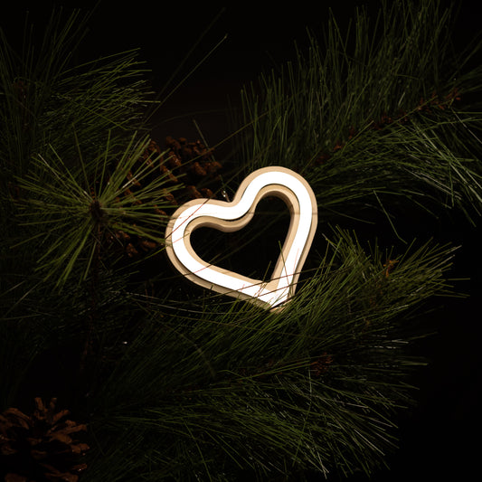 Cool white neon heart ornament hanging on a Christmas tree with pine branches and pine cones - LED neon holiday decor by Our Glowing Hearts