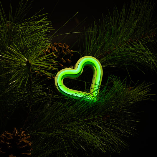 Green neon heart ornament hanging on a Christmas tree with pine branches and pine cones - LED neon holiday decor by Our Glowing Hearts
