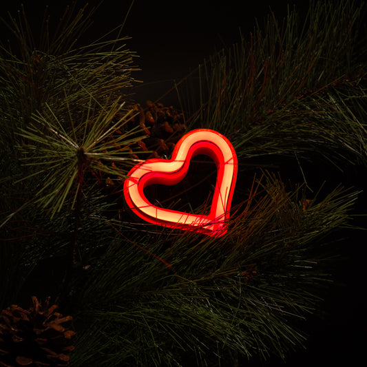 Red neon heart ornament hanging on a Christmas tree with pine branches and pine cones - LED neon holiday decor by Our Glowing Hearts