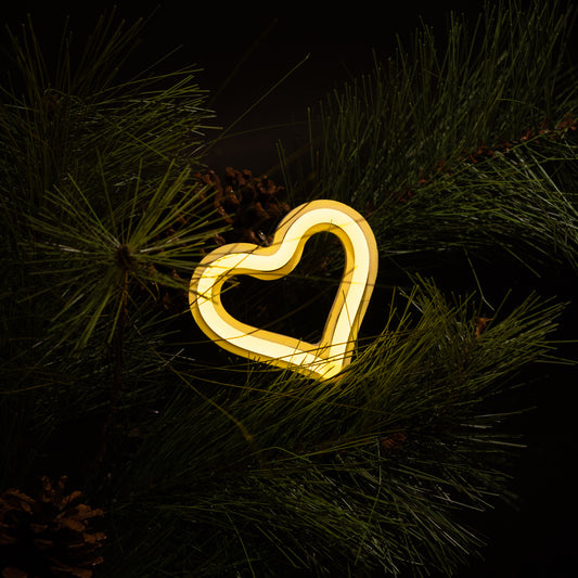 Yellow neon heart ornament hanging on a Christmas tree with pine branches and pine cones - LED neon holiday decor by Our Glowing Hearts