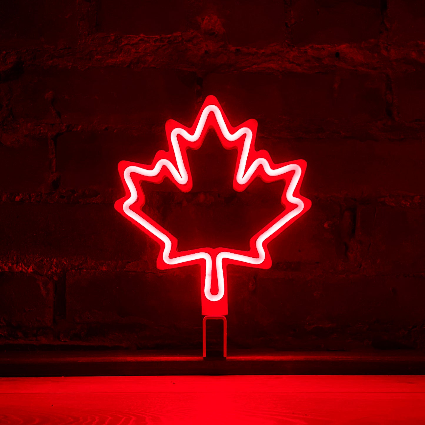 Red neon maple leaf art glowing against a brick wall - LED neon maple leaf light by Our Glowing Hearts handmade in Canada