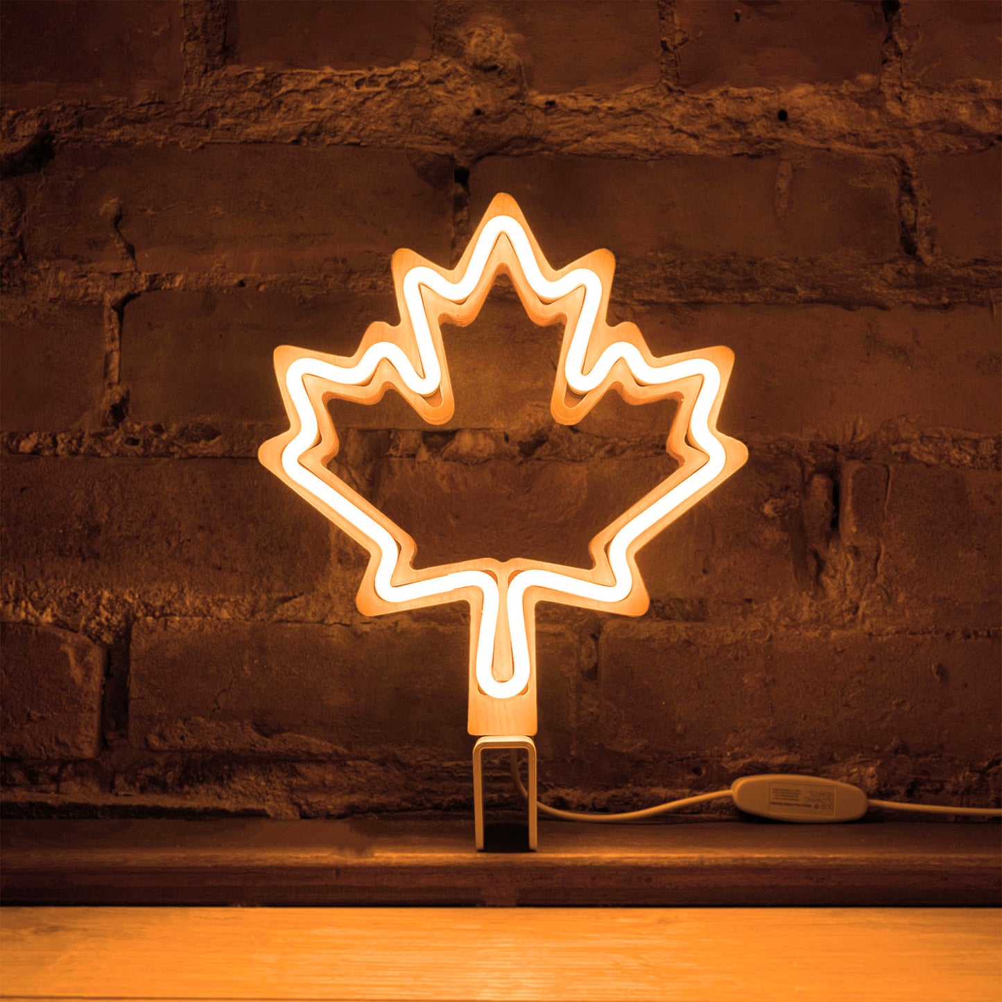 Warm white neon maple leaf art glowing against a brick wall - LED neon maple leaf light by Our Glowing Hearts handmade in Canada