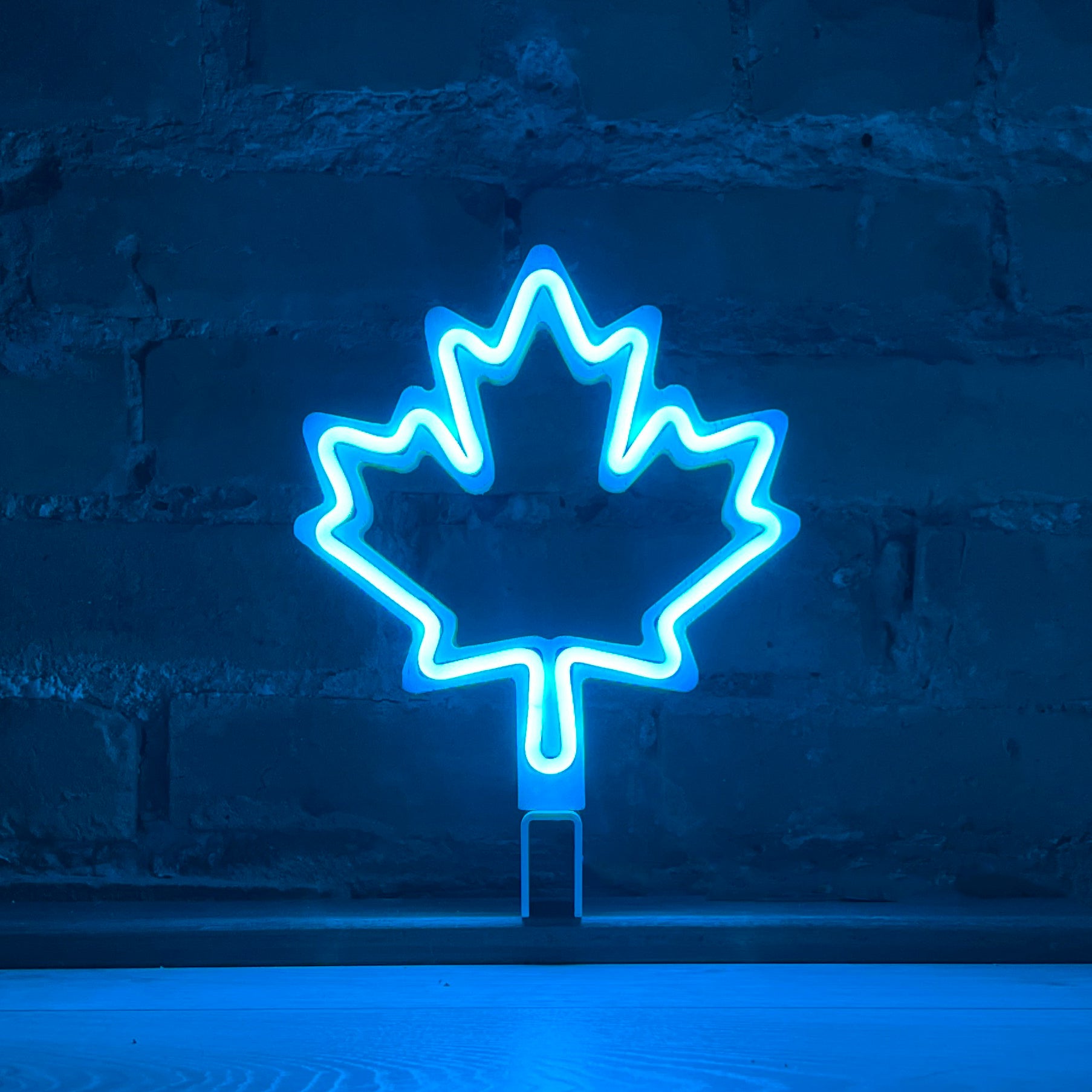 Cyan neon maple leaf art glowing against a brick wall - LED neon maple leaf light by Our Glowing Hearts handmade in Canada