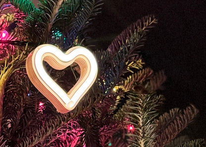LED neon heart ornament hanging on a Christmas tree with colorful lights - handmade neon heart holiday decor by Our Glowing Hearts
