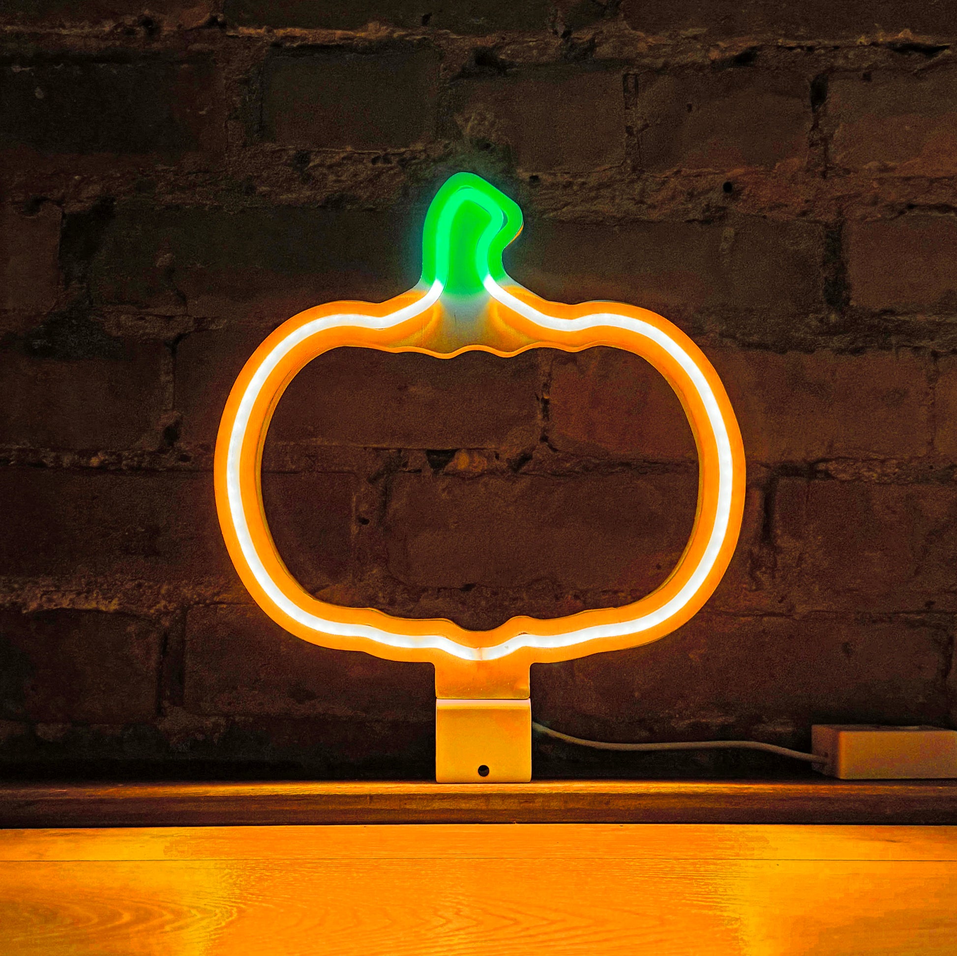 The Glowing Pumpkin neon art in orange and green glowing against a brick wall - LED neon pumpkin light for Halloween and autumn decor by Our Glowing Hearts handmade in Canada