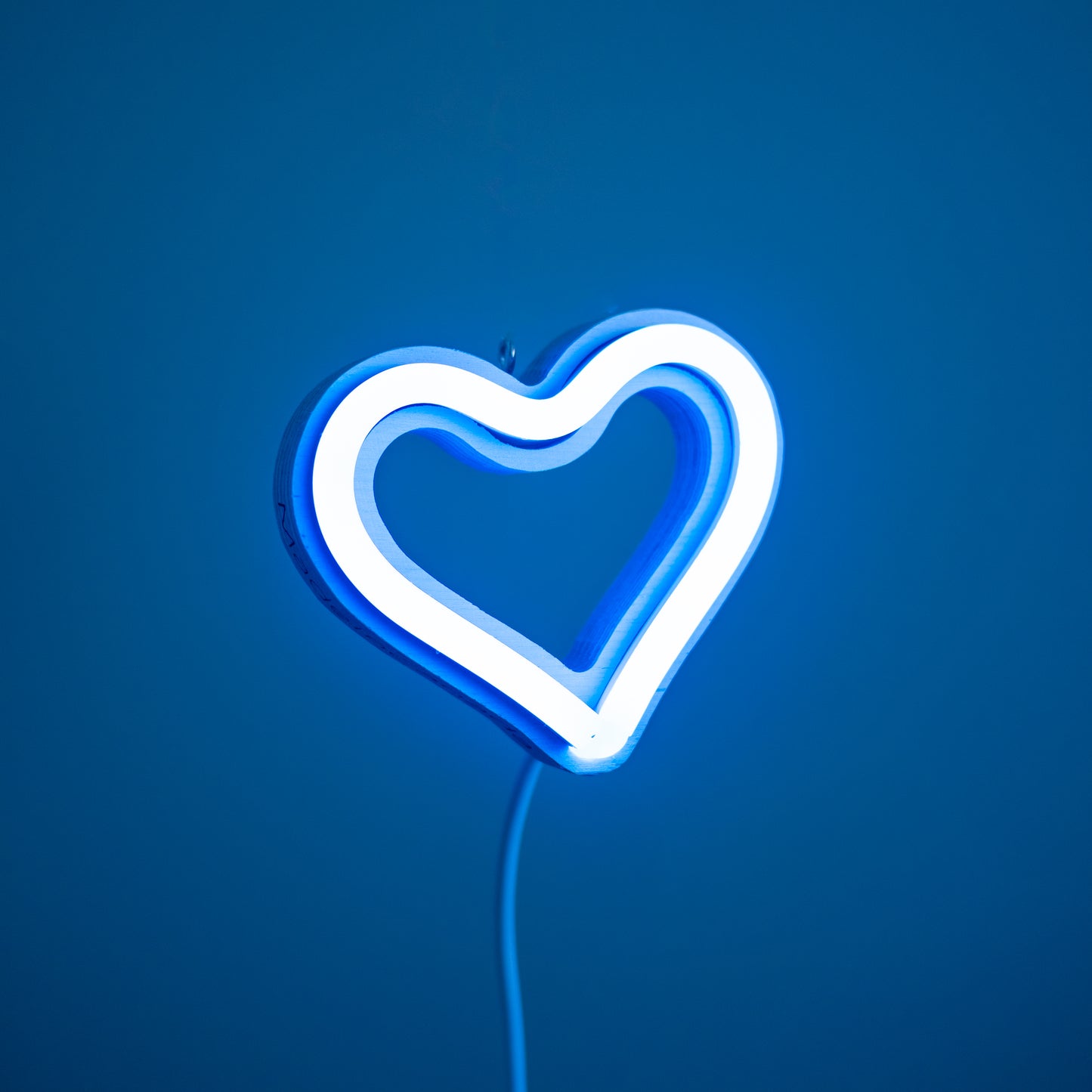 Front view of cyan neon heart ornament with hanging hook glowing against a blue background - 3 inch LED neon heart light by Our Glowing Hearts