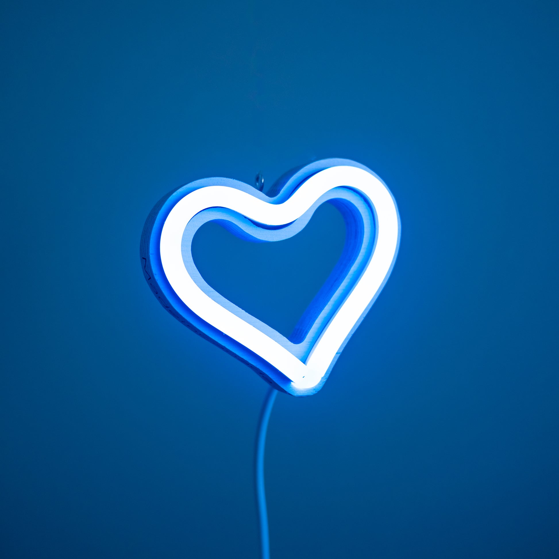 Front view of cyan neon heart ornament with hanging hook glowing against a blue background - 3 inch LED neon heart light by Our Glowing Hearts