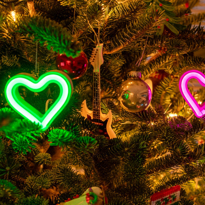 Green and magenta LED neon heart ornaments on a decorated Christmas tree with festive ornaments and lights by Our Glowing Hearts