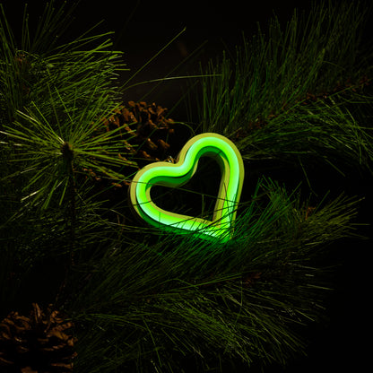 Green neon heart ornament hanging on a Christmas tree with pine branches and pine cones - LED neon holiday decor by Our Glowing Hearts