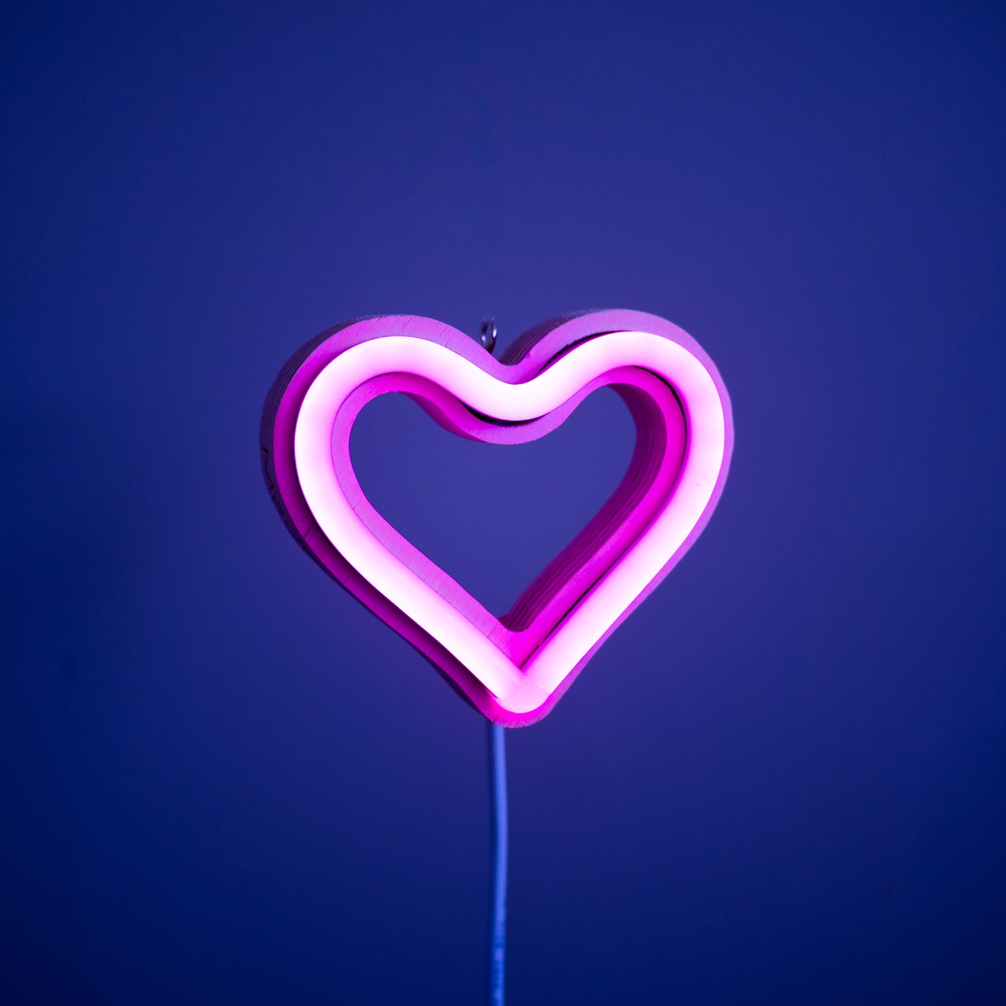 Front view of magenta neon heart ornament with hanging hook glowing against a blue background - 3 inch LED neon heart light by Our Glowing Hearts