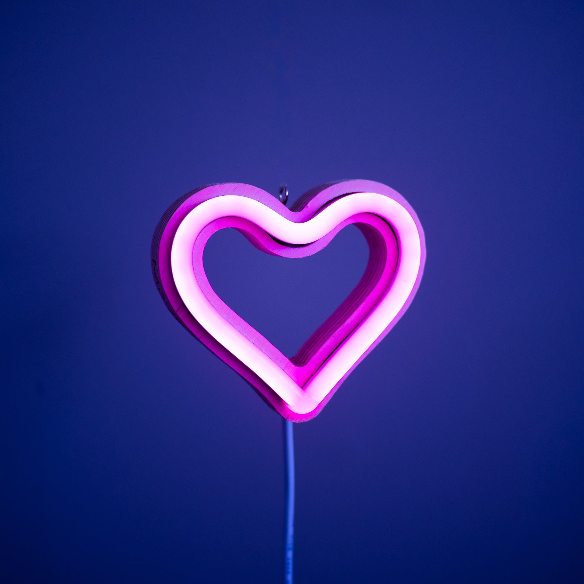 Front view of magenta neon heart ornament with hanging hook glowing against a blue background - 3 inch LED neon heart light by Our Glowing Hearts