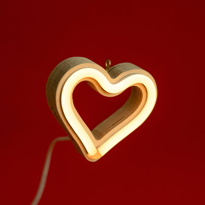 Front view of warm white neon heart ornament with hanging hook glowing against a red background - 3 inch LED neon heart light by Our Glowing Hearts