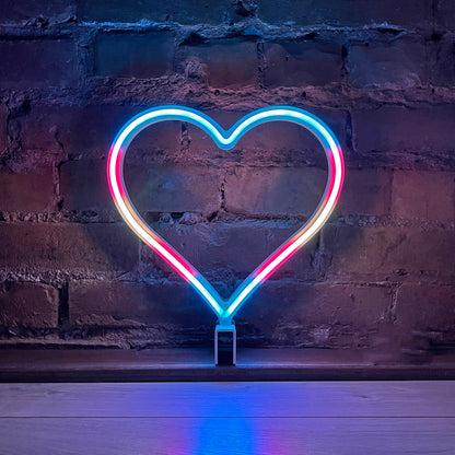 Neon Queer Heart art in transgender pride flag colors glowing against a brick wall - 12 inch LED neon heart light with 12 pride flag modes by Our Glowing Hearts, handmade in Canada
