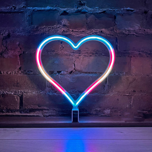 Neon Queer Heart art in transgender pride flag colors glowing against a brick wall - 12 inch LED neon heart light with 12 pride flag modes by Our Glowing Hearts, handmade in Canada