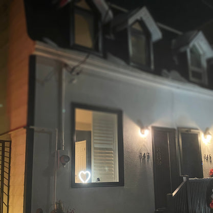Cool white neon heart art glowing in a home window at night visible from the street - LED neon heart window decor spreading love in the neighborhood by Our Glowing Hearts