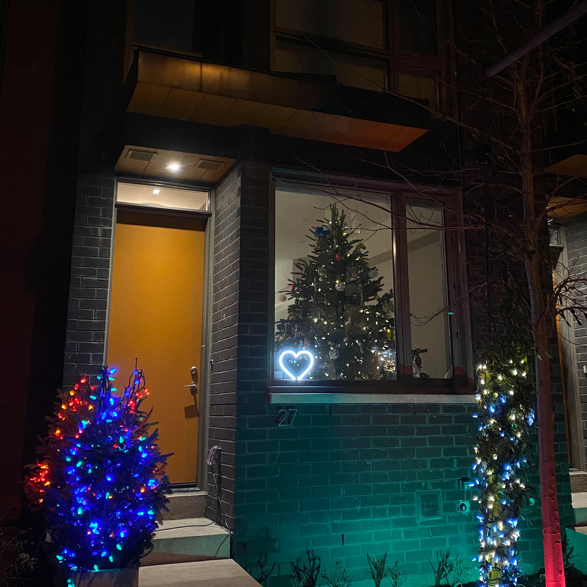Cool white neon heart art glowing in a front window surrounded by festive Christmas lights and holiday decorations - LED neon heart perfect for seasonal window display by Our Glowing Hearts