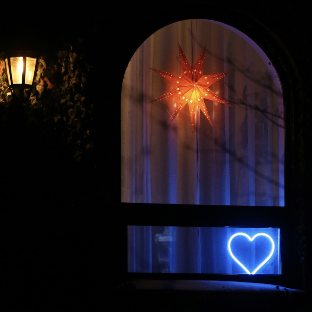 Cyan neon heart art displayed in a home window at night beneath a decorative star - LED neon heart window decor creating a warm community glow by Our Glowing Hearts