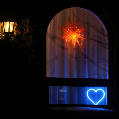 Cyan neon heart art displayed in a home window at night beneath a decorative star - LED neon heart window decor creating a warm community glow by Our Glowing Hearts