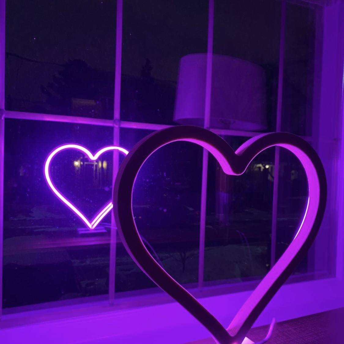 Magenta neon heart art displayed in a window at night with a glowing reflection - LED neon heart wall decor by Our Glowing Hearts