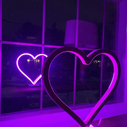 Magenta neon heart art displayed in a window at night with a glowing reflection - LED neon heart wall decor by Our Glowing Hearts