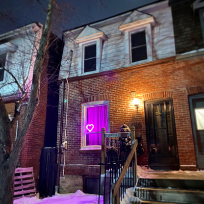 Pink neon heart art glowing in a home window at night on a brick house - LED heart-shaped light spreading love in the neighborhood by Our Glowing Hearts, handmade in Canada