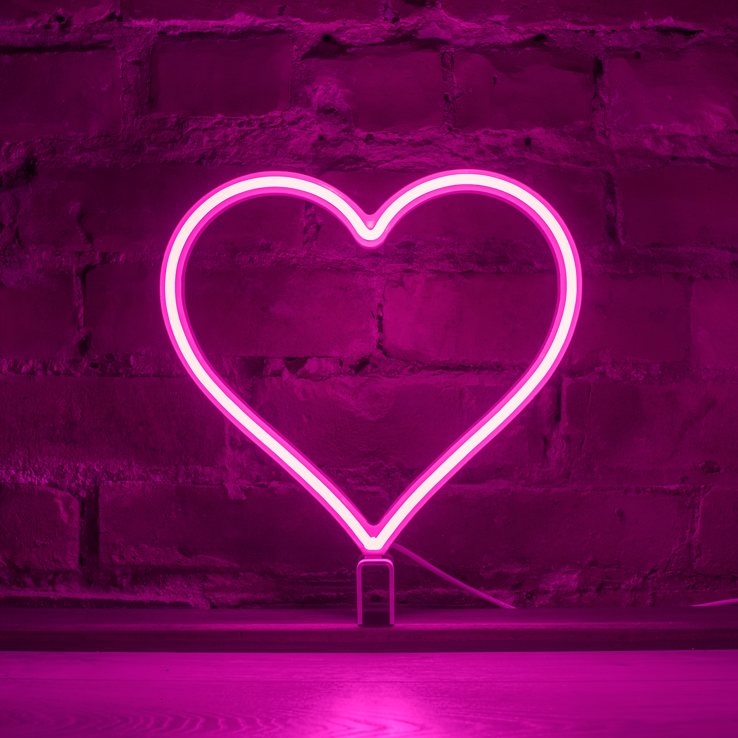 Pink neon heart art glowing against a brick wall - 12 inch LED neon heart light by Our Glowing Hearts, handmade in Canada