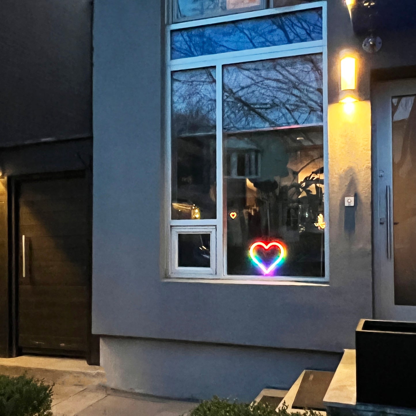 Rainbow neon heart art glowing in a home window seen from outside at night - LED neon heart window display adding curb appeal by Our Glowing Hearts