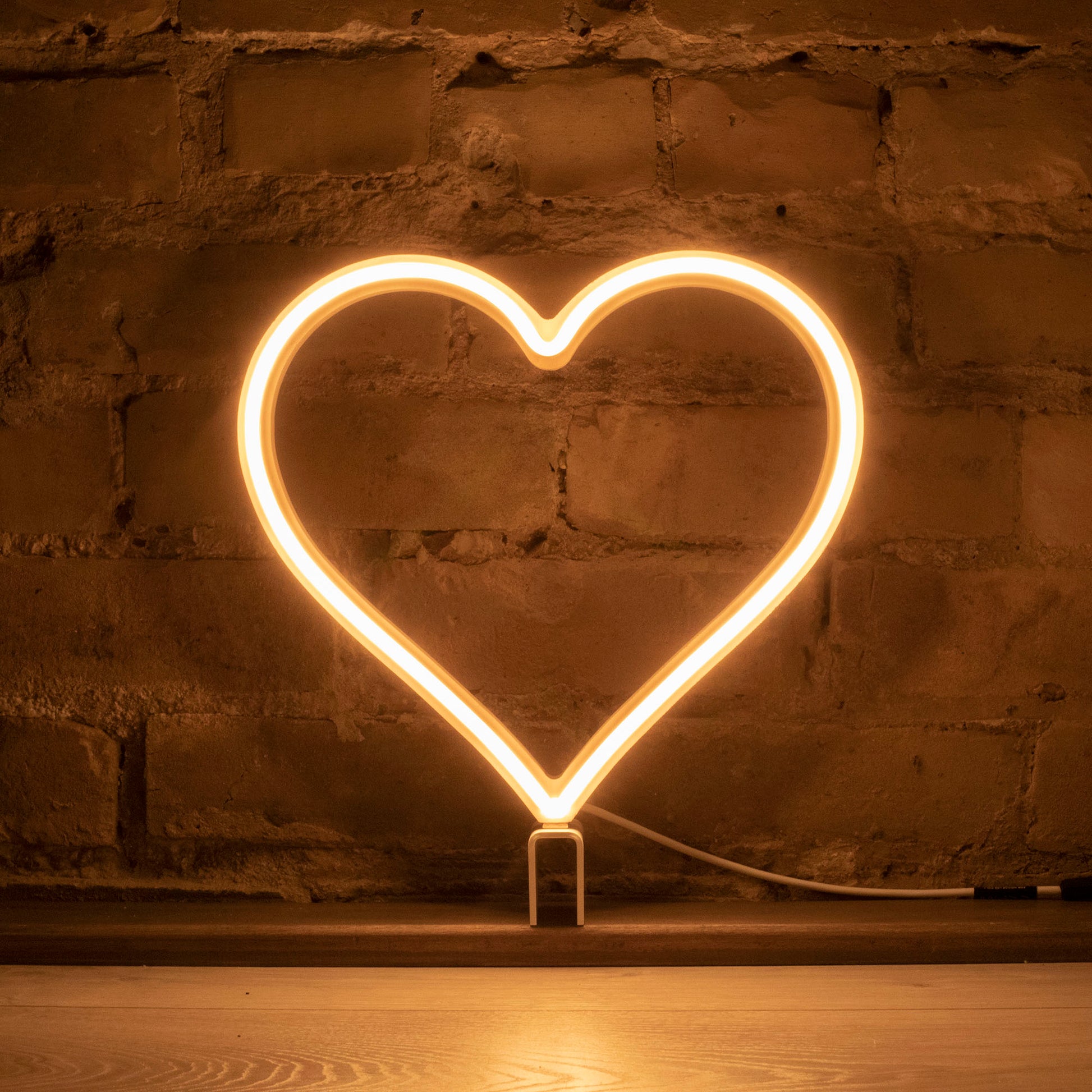 Warm white neon heart art glowing against a brick wall - 12 inch LED neon heart light with warm amber glow by Our Glowing Hearts, handmade in Canada
