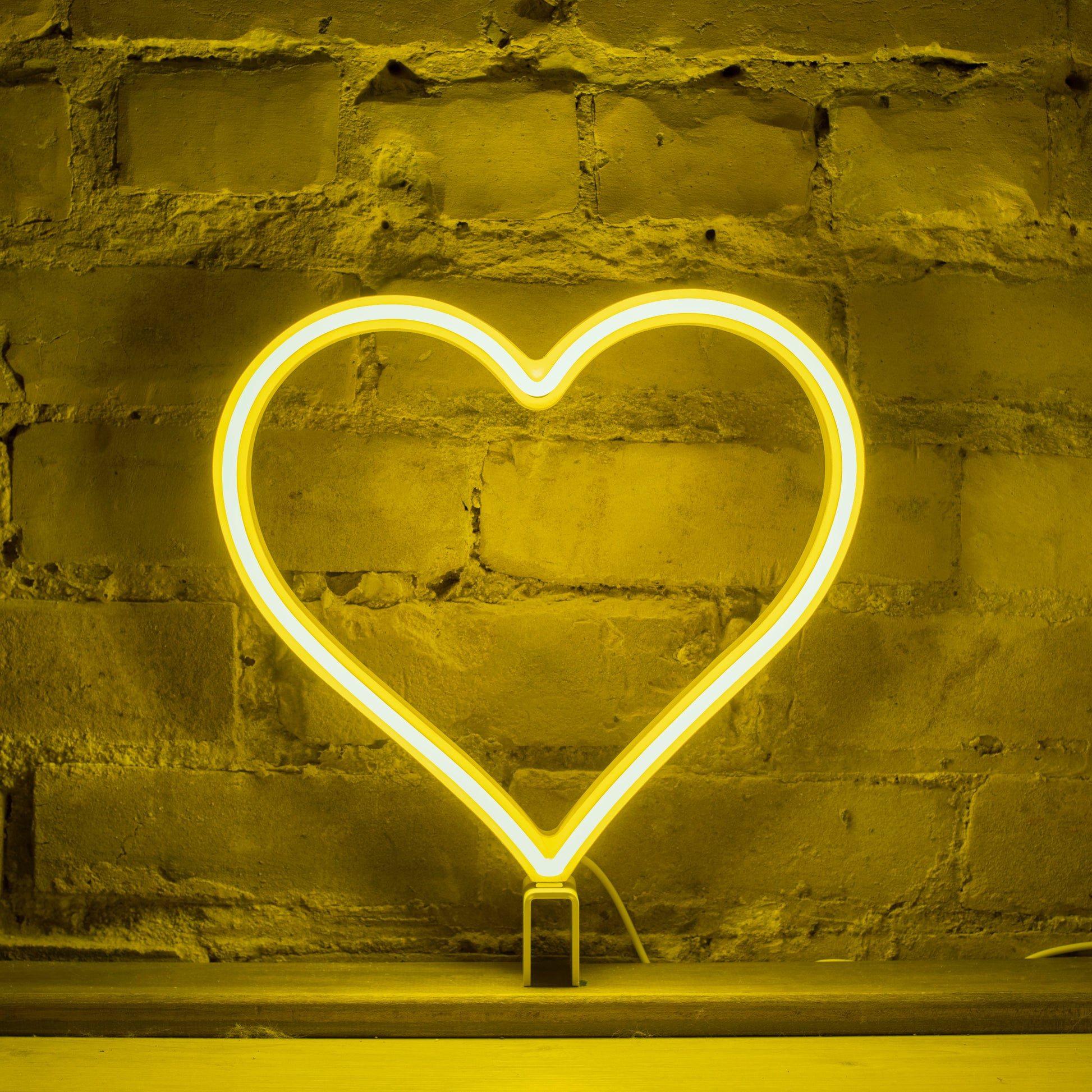 Yellow neon heart art glowing against a brick wall - 12 inch LED neon heart light by Our Glowing Hearts, handmade in Canada