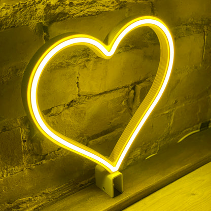 Yellow neon heart art glowing from a side angle against a brick wall - 12 inch LED neon heart light on steel baseplate by Our Glowing Hearts